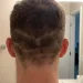 Rear view of a person's head showing a botched DIY haircut with multiple uneven, horizontal fade lines and patchy lengths in a home bathroom setting.