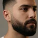 : Close-up portrait of a man with a clean low beard fade, blending short sideburns into a full beard.