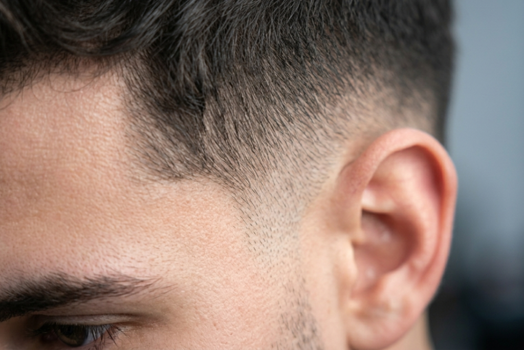 Macro close-up of a precision low taper fade showing the blend at the temple and sideburns with detailed hair texture.